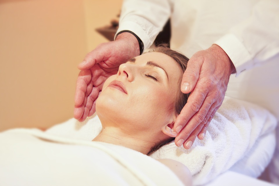 mujer en camilla mientras terapeuta de la da reiki con mano a lado de las orejas