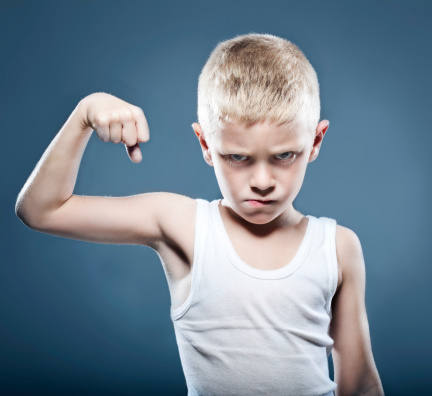 niño con aspecto agresivo haciendo bicep para demostrar fuerza