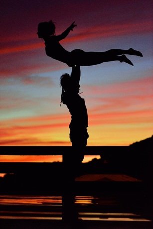 hombre y mujer practicando acroyoga al atardecer en la playa
