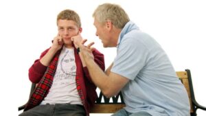 padre hablando con su hijo adolescente que se pone los dedos en los oídos para no escucharle