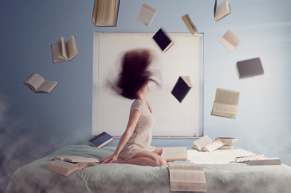 mujer sentada en una cama lanzando libros al aire