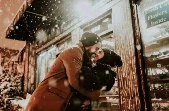 hombre y mujer se abrazan por la calle bajo la nieve