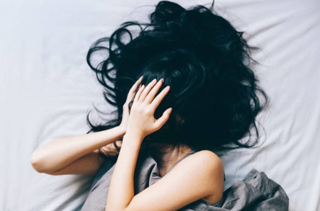 mujer tumbada en la cama con cara cubierta por el pelo y las manos, asustada