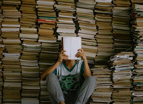 montaña de libros apilados y chico delante leyendo uno