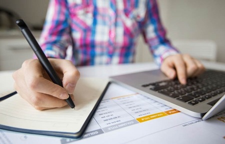 persona trabajando con laptop y apuntando objetivos en cuaderno