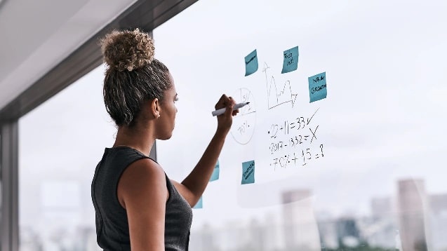 chica escribiendo en cristal objetivos y post it