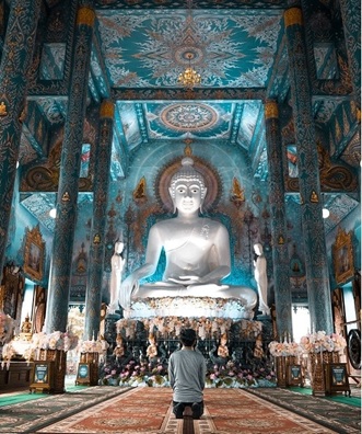 hombre rezando dentro templo con gran Buda en piedra caliza